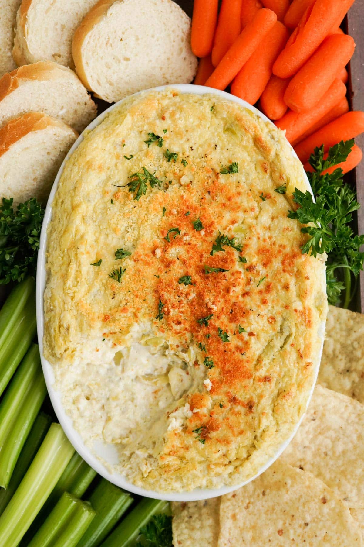 artichoke dip in a white dish with carrots, celery and bread
