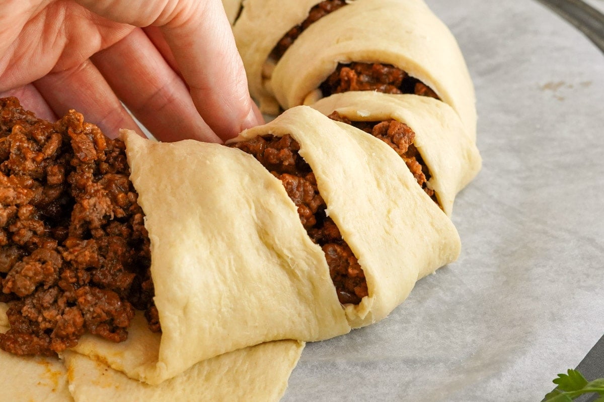 hand pulling up triangles of crescent dough over taco meat for a taco ring