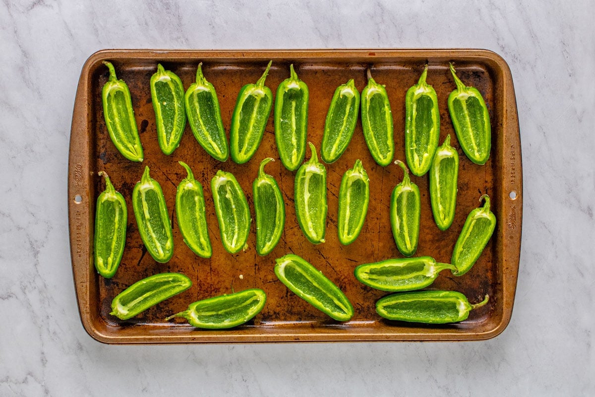 jalapenos sliced in half and arranged on a baking sheet