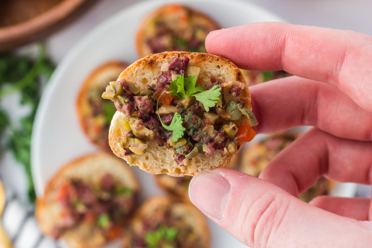 hand holding a crostini slice with olive tapenade