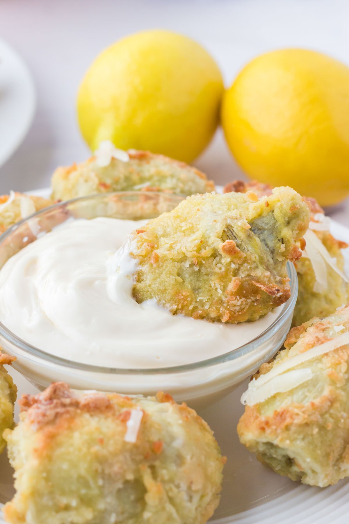 fried artichoke hearts, a bowl of creamy white dip, lemons