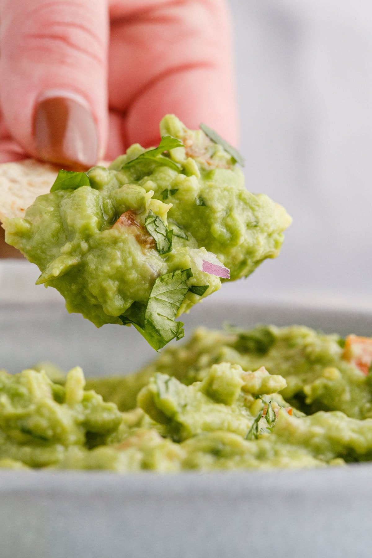a hand holding a chip with guacamole