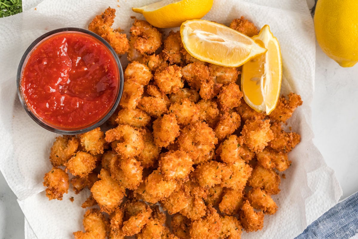a big batch of popcorn shrimp over paper towels, with lemons and cocktail sauce
