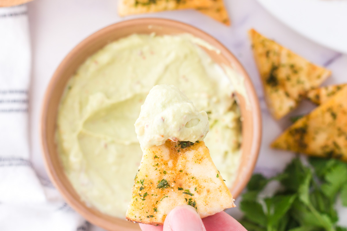 hand holding a pit chip with avocado dip