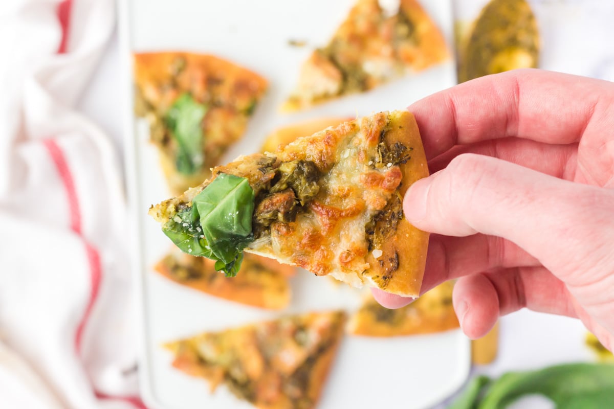 slice of flatbread pizza with basil, chicken, pesto and cheese