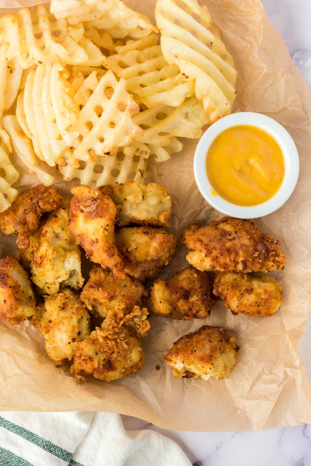 Copycat Chick-Fil-A Chicken Nuggets and waffle fries with a mustard sauce sitting on a pieces of brown paper. 