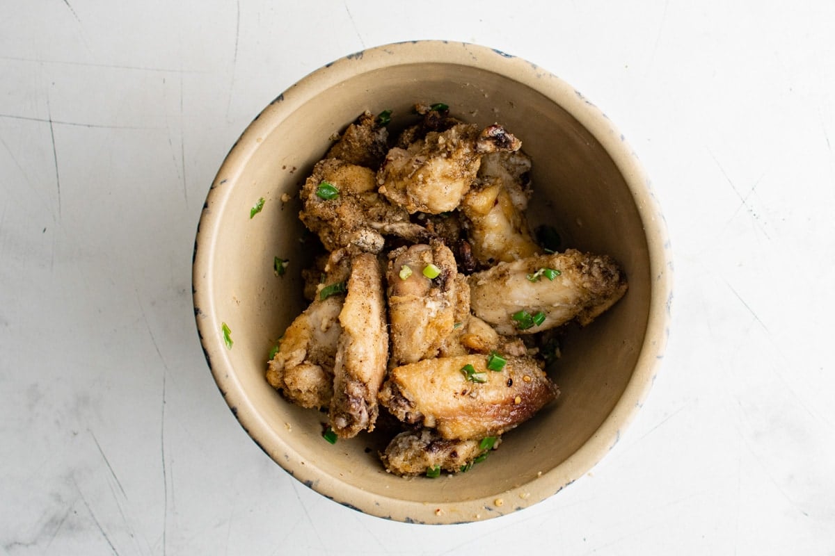Crispy baked chicken wings in a bowl with salt and pepper garlic sauce and sliced green onions. 
