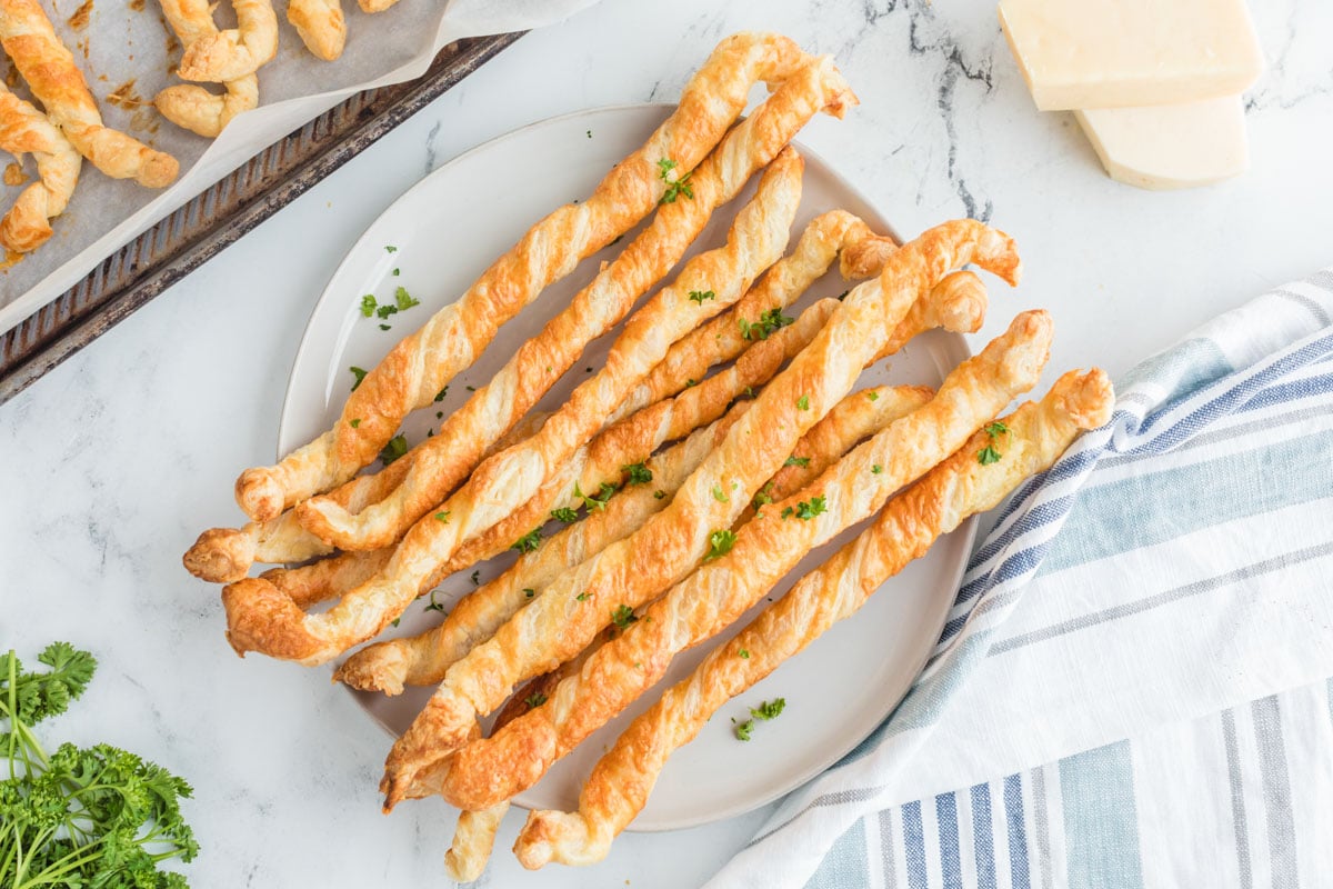 A stack of crispy cheese straws on a white plate.