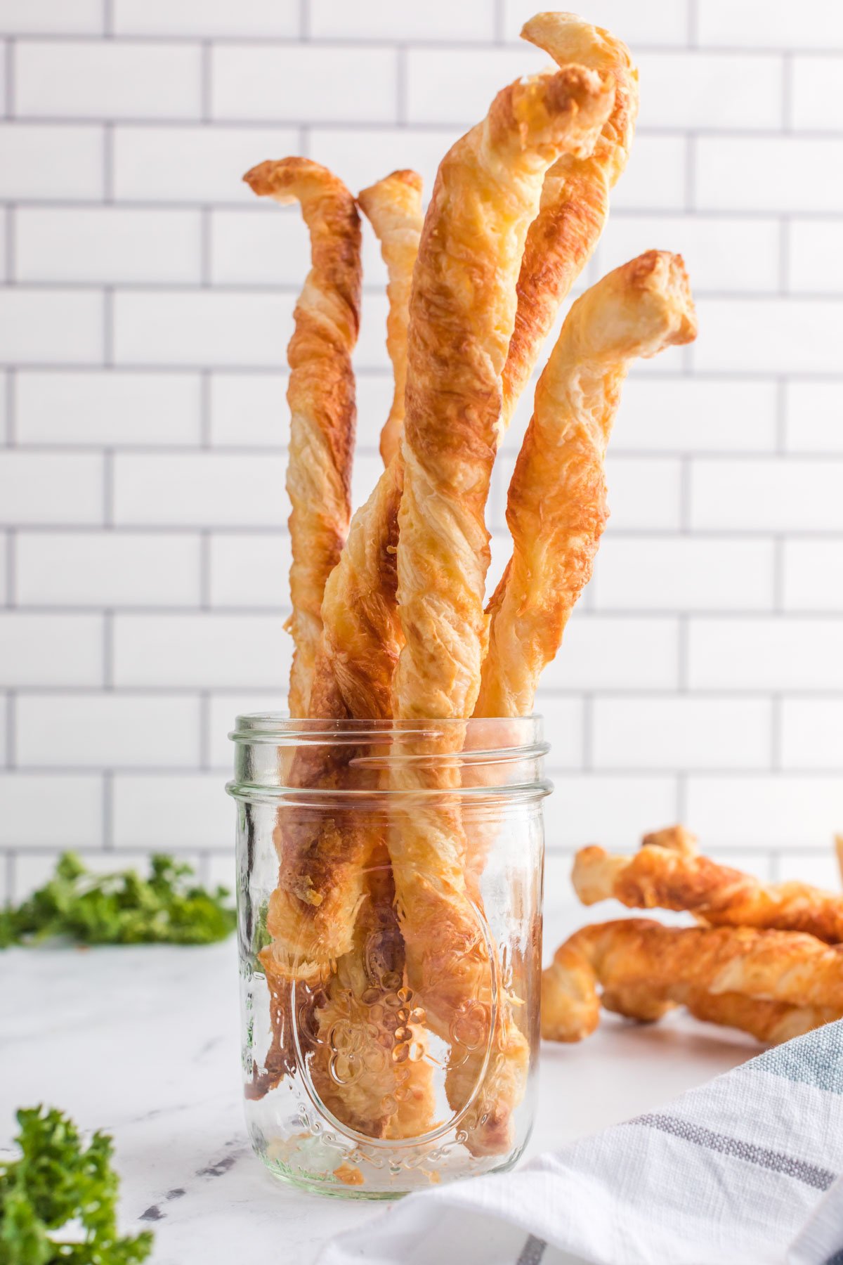 Puff pastry cheese straws standing up in a clear glass jar. 