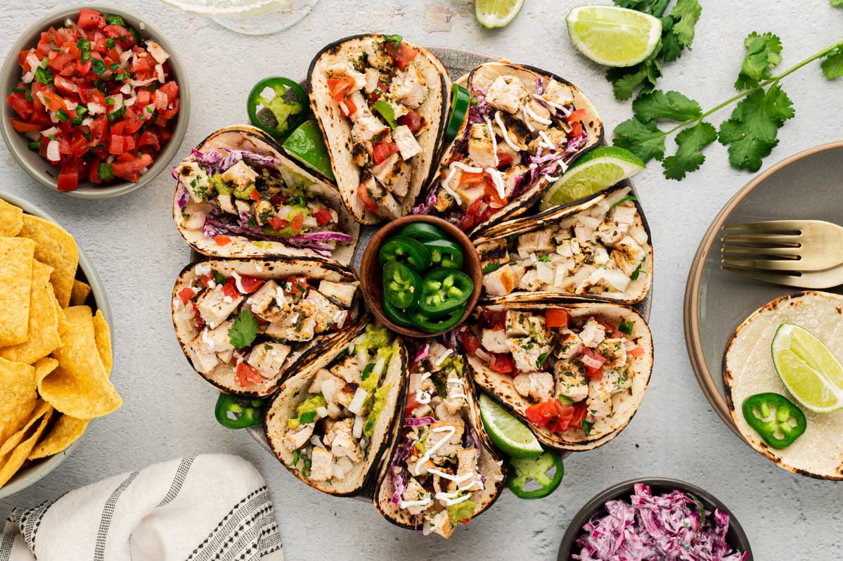 Chicken tacos on a round platter surrounded by toppings. 