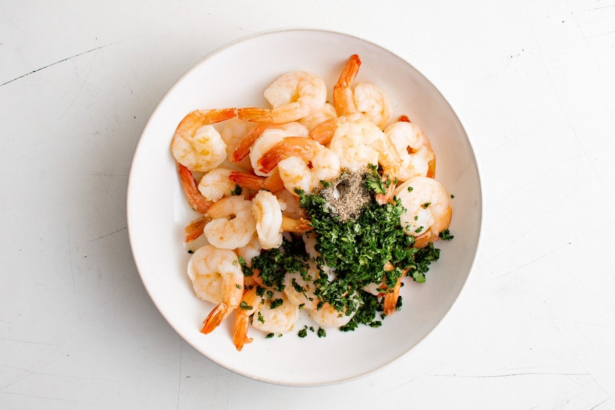 Cooked shrimp, lime juice and cilantro in a large white bowl. 