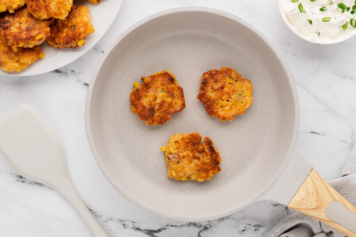 Mini corn cakes fried in a skillet. 