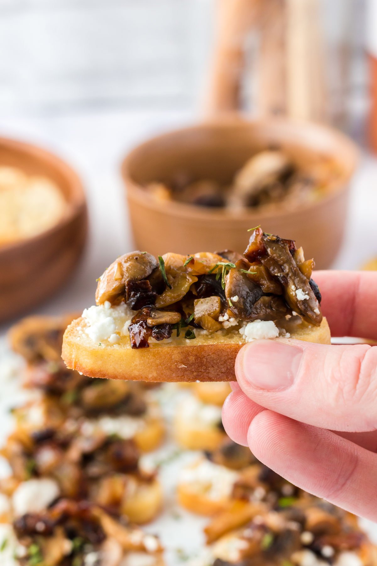 A hand holding a crostini with mushrooms and goat cheese. 