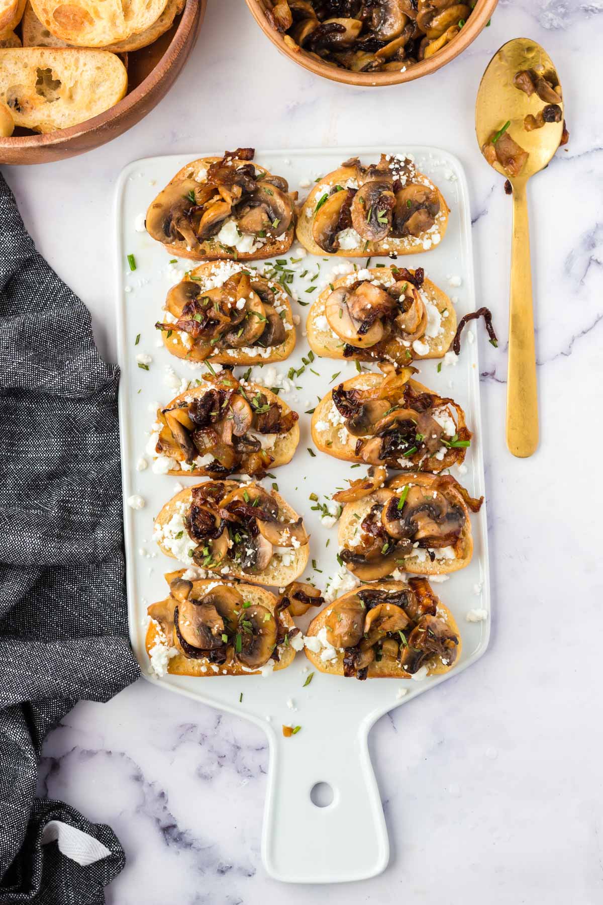Crostini with goat cheese and mushrooms on a white cutting board. 
