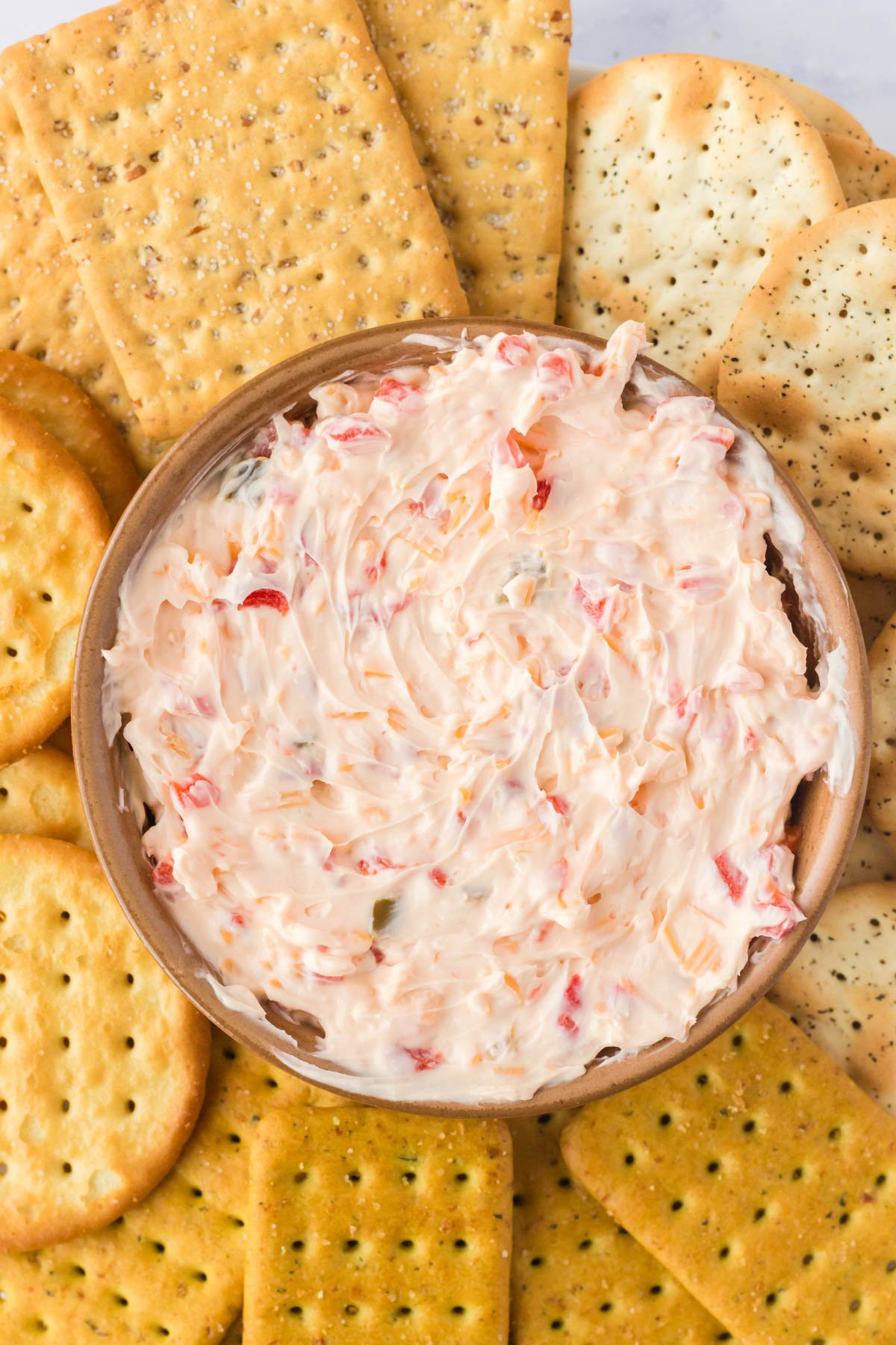 pimento cheese spread in a bowl surround by a variety of crackers.