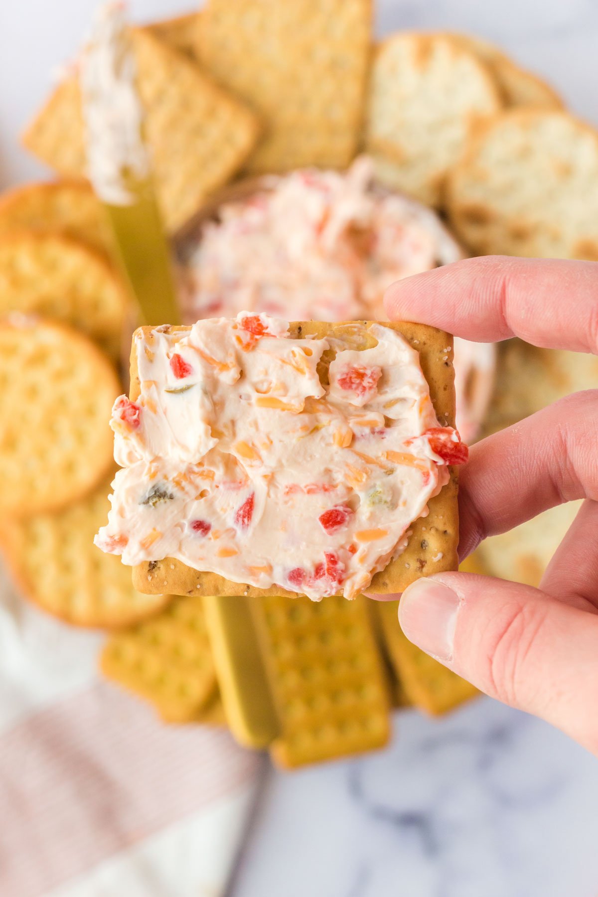 A hand holding a cracker spread with pimento cheese. 
