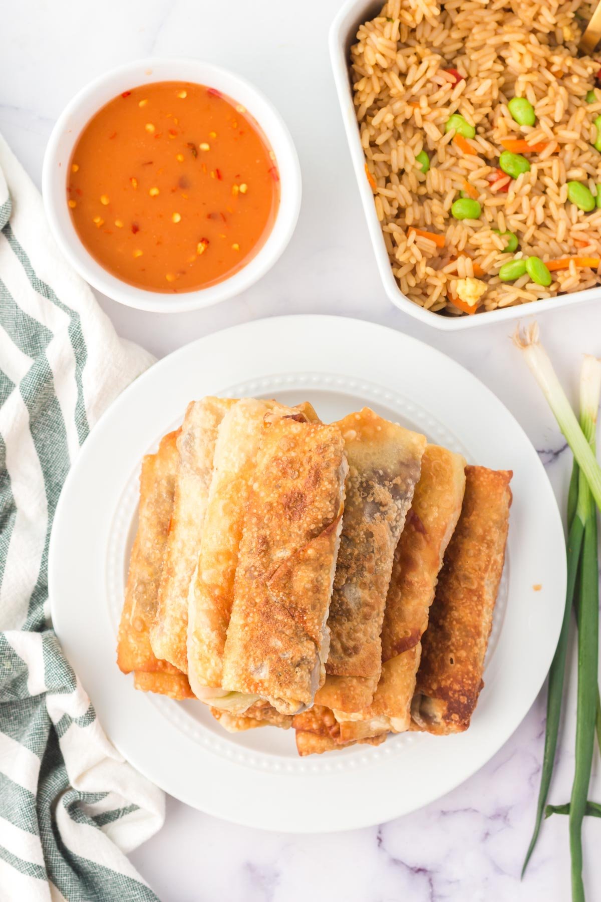 fried egg rolls on a plate, a dish of sweet and sour sauce and a plate of fried rice.
