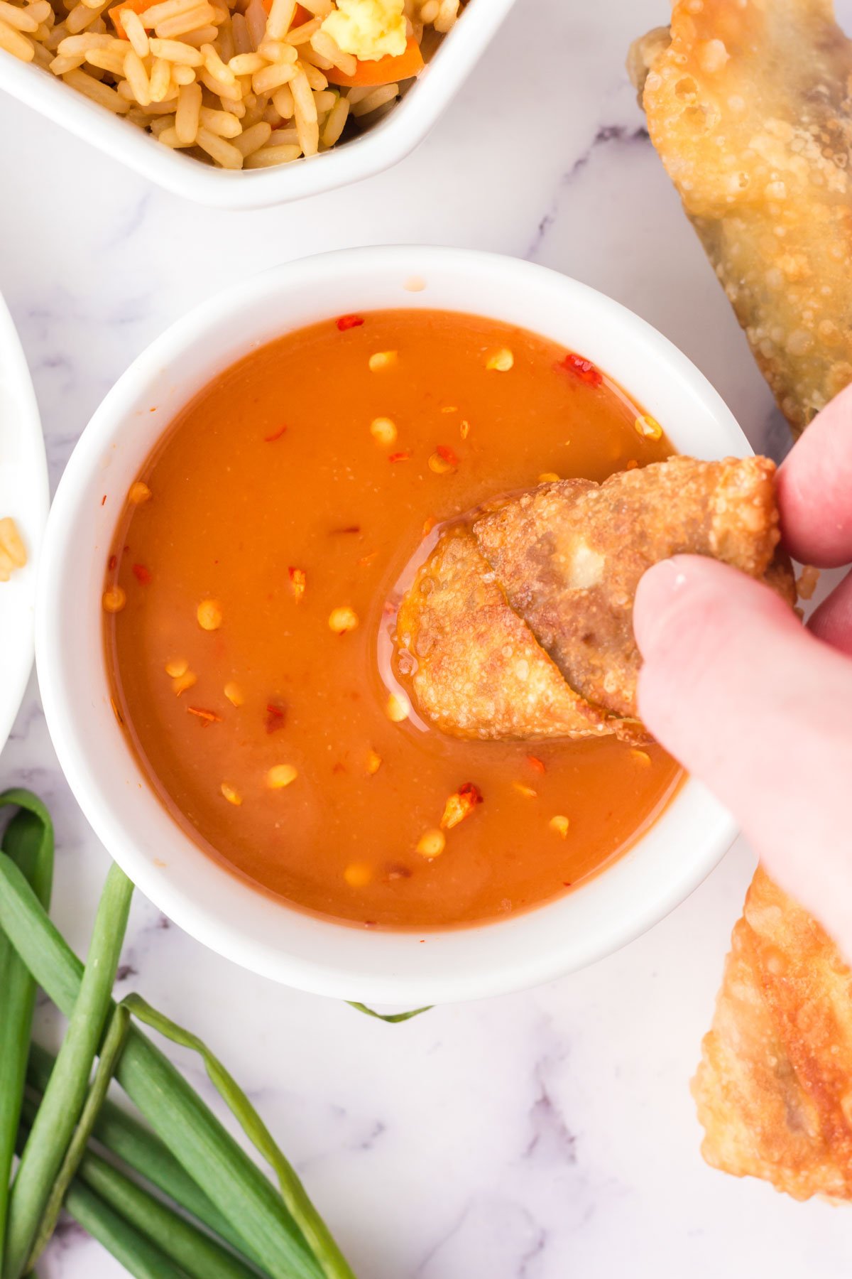 A hand is dipping a vegetable egg roll into a dish of sweet and sour sauce.