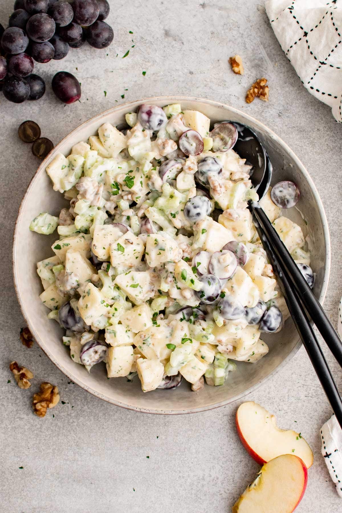 A white serving bowl filled with waldorf salad and two large serving spoons. 