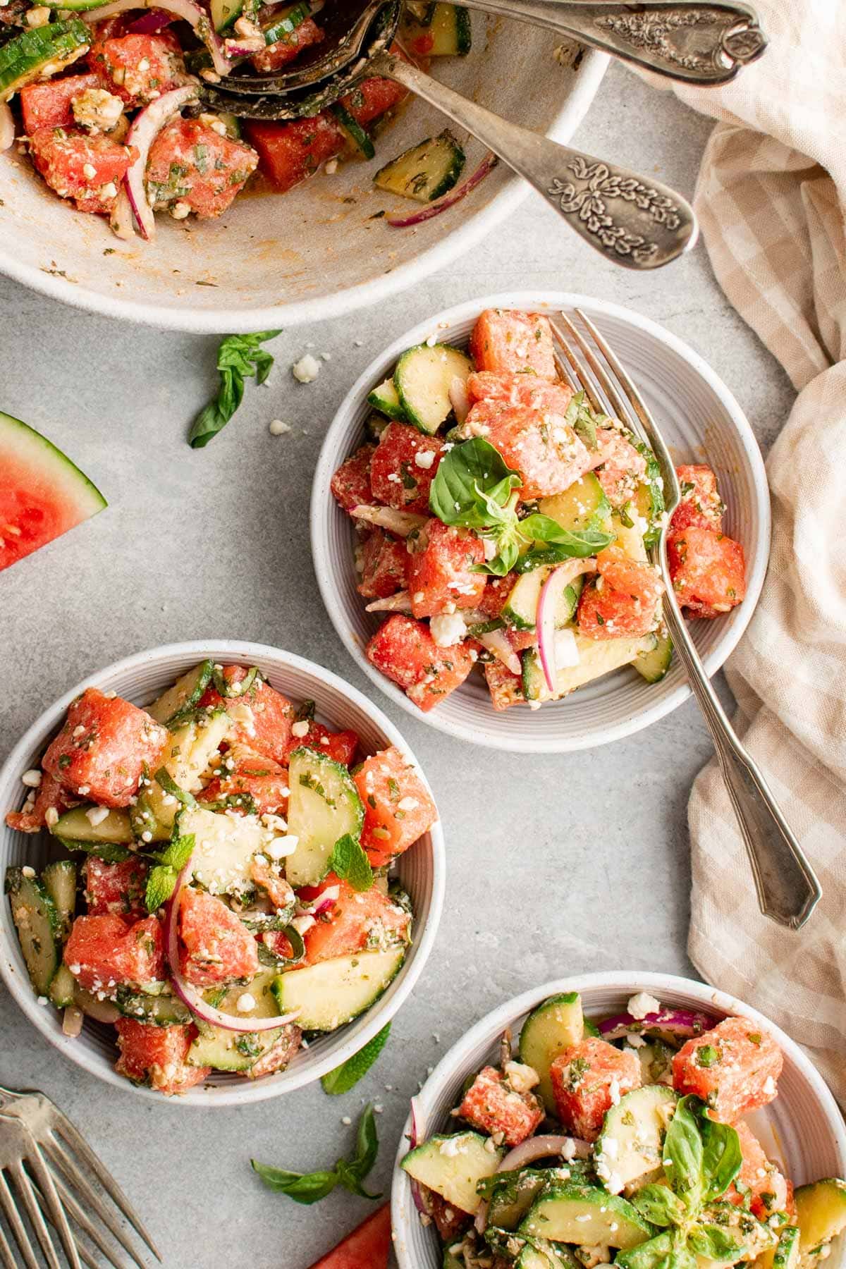 Small white bowls with servings of watermelon salad with feta and cucumbers.