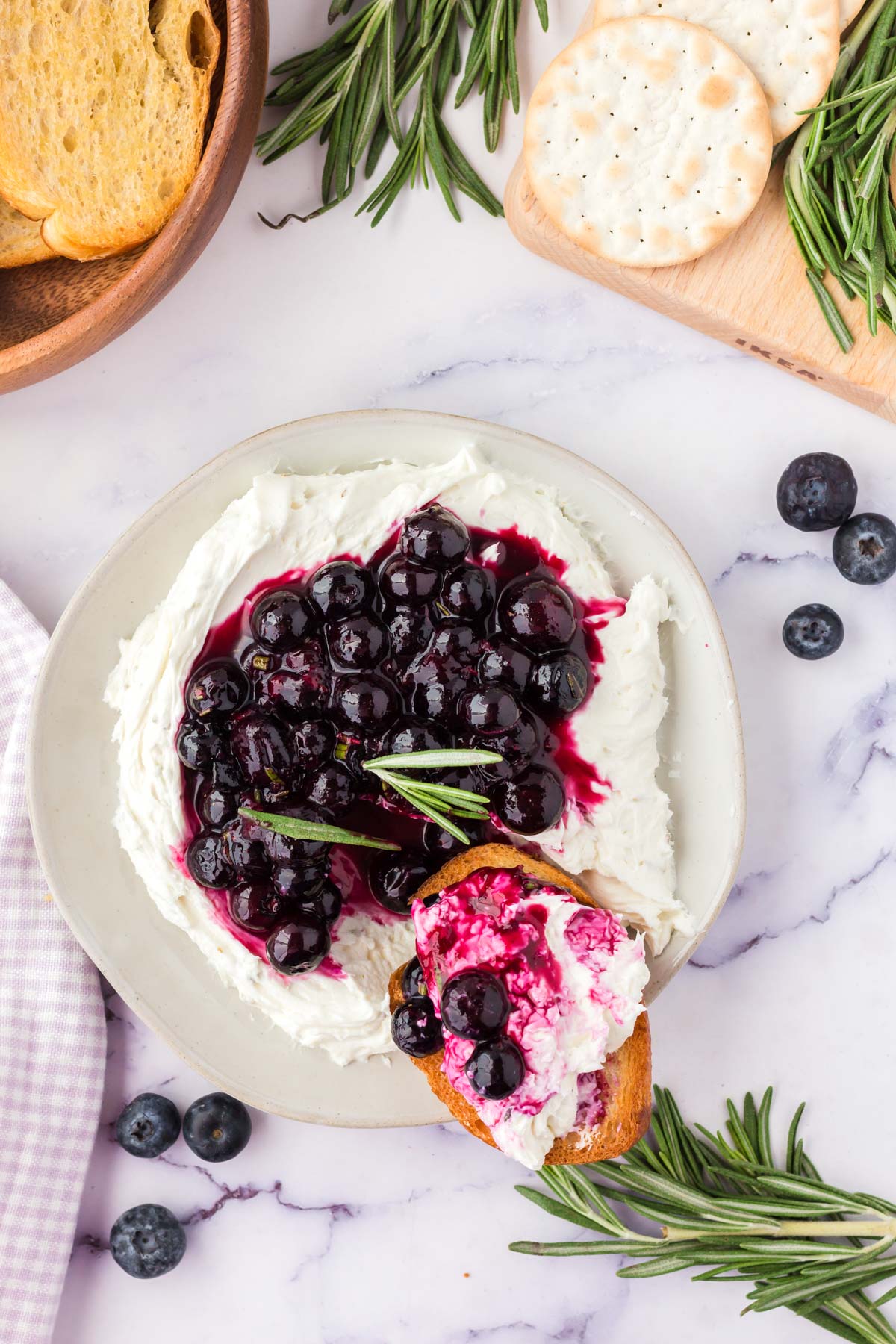 Goat cheese with blueberry topping, rosemary, crackers on white platters.