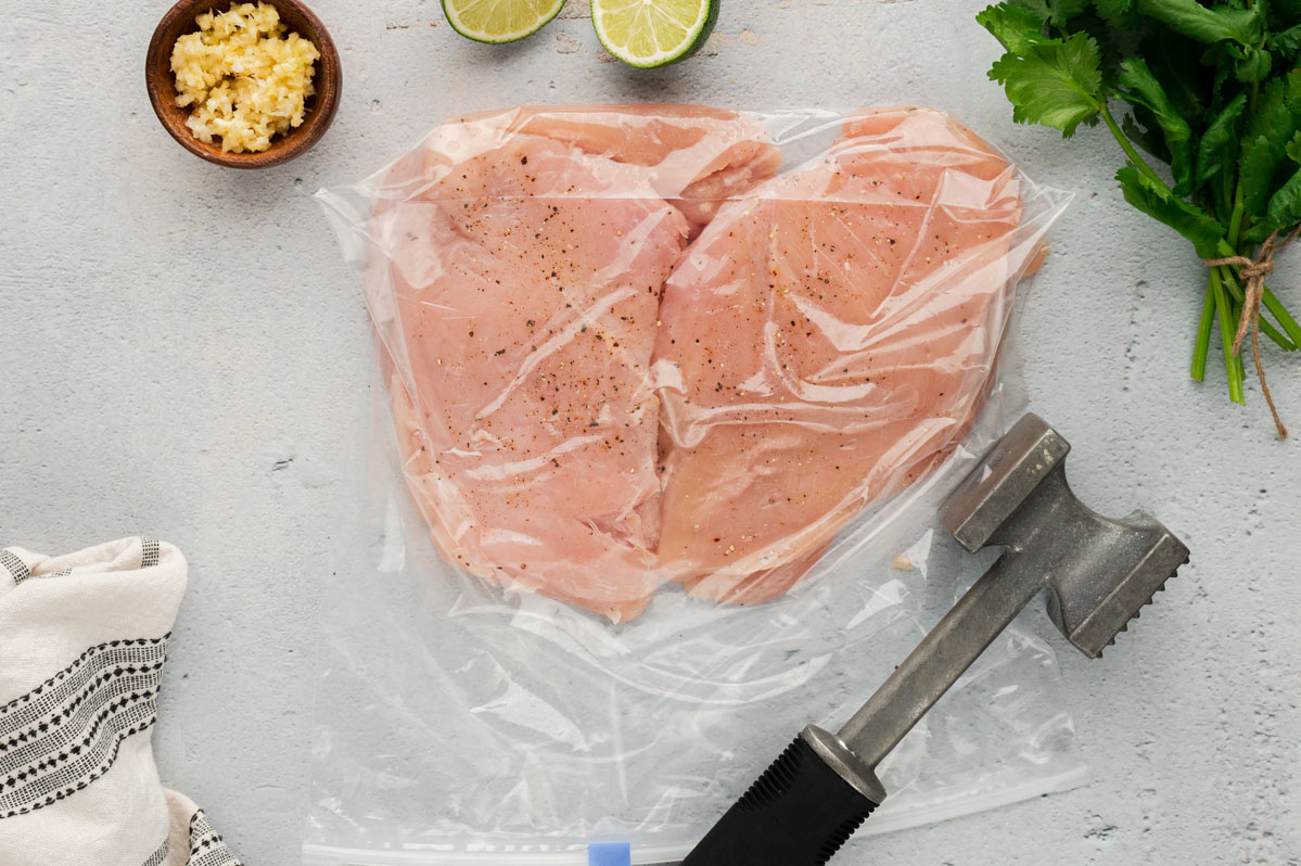 chicken breasts in a clear plastic bag with a meat mallet for pounding.
