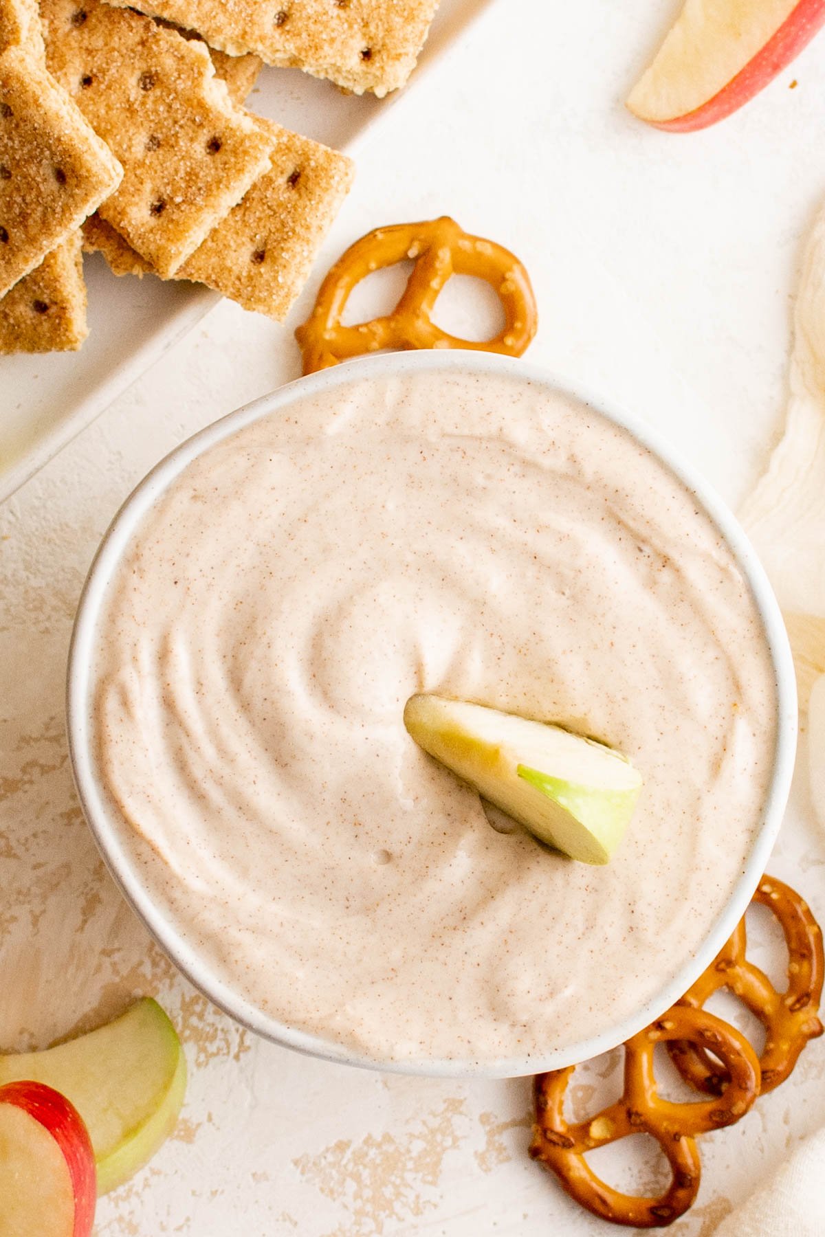 A bowl of cream cheese fruit dip, with a sliced apple in it. 