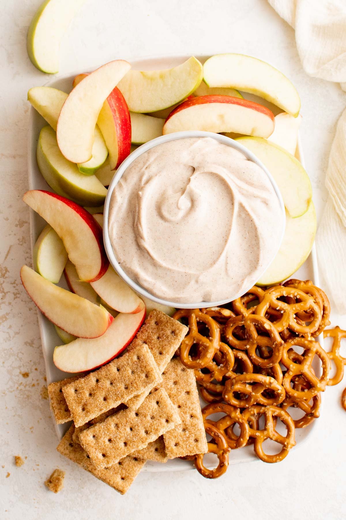A large platter with sliced apples, pretzels, graham crackers and a bowl of cream cheese apple dip. 