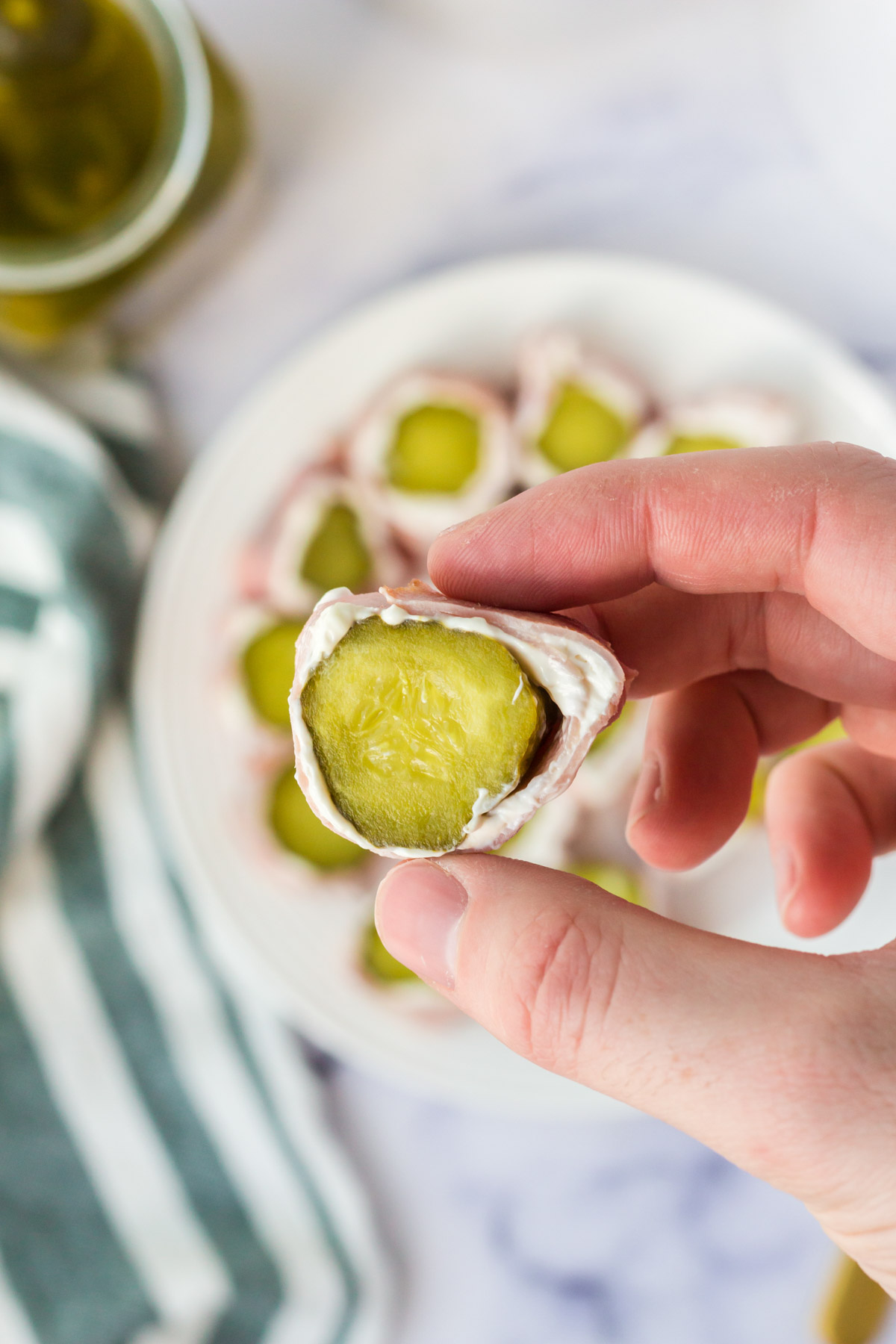A hand holding a pickle roll up with ham. 