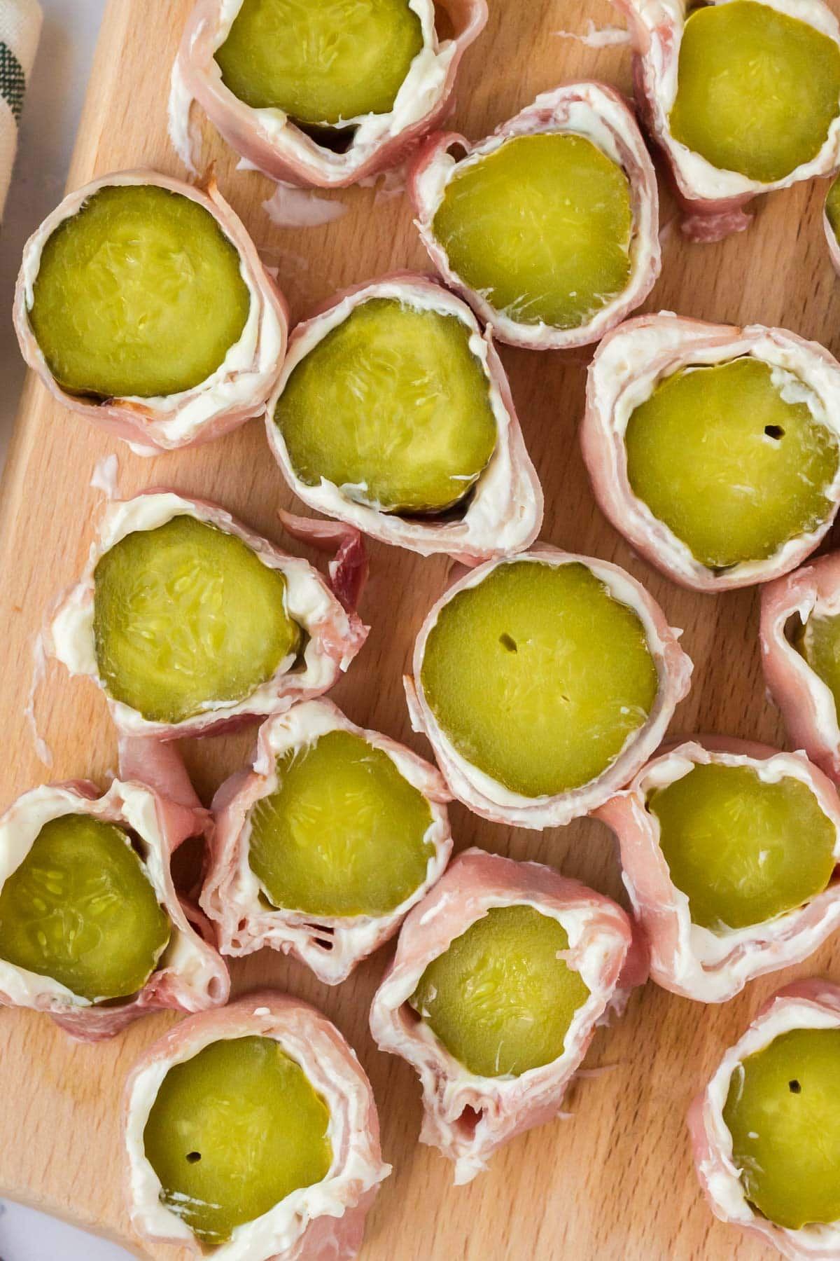 Pickle ham and cream cheese roll ups on a wood cutting board. 