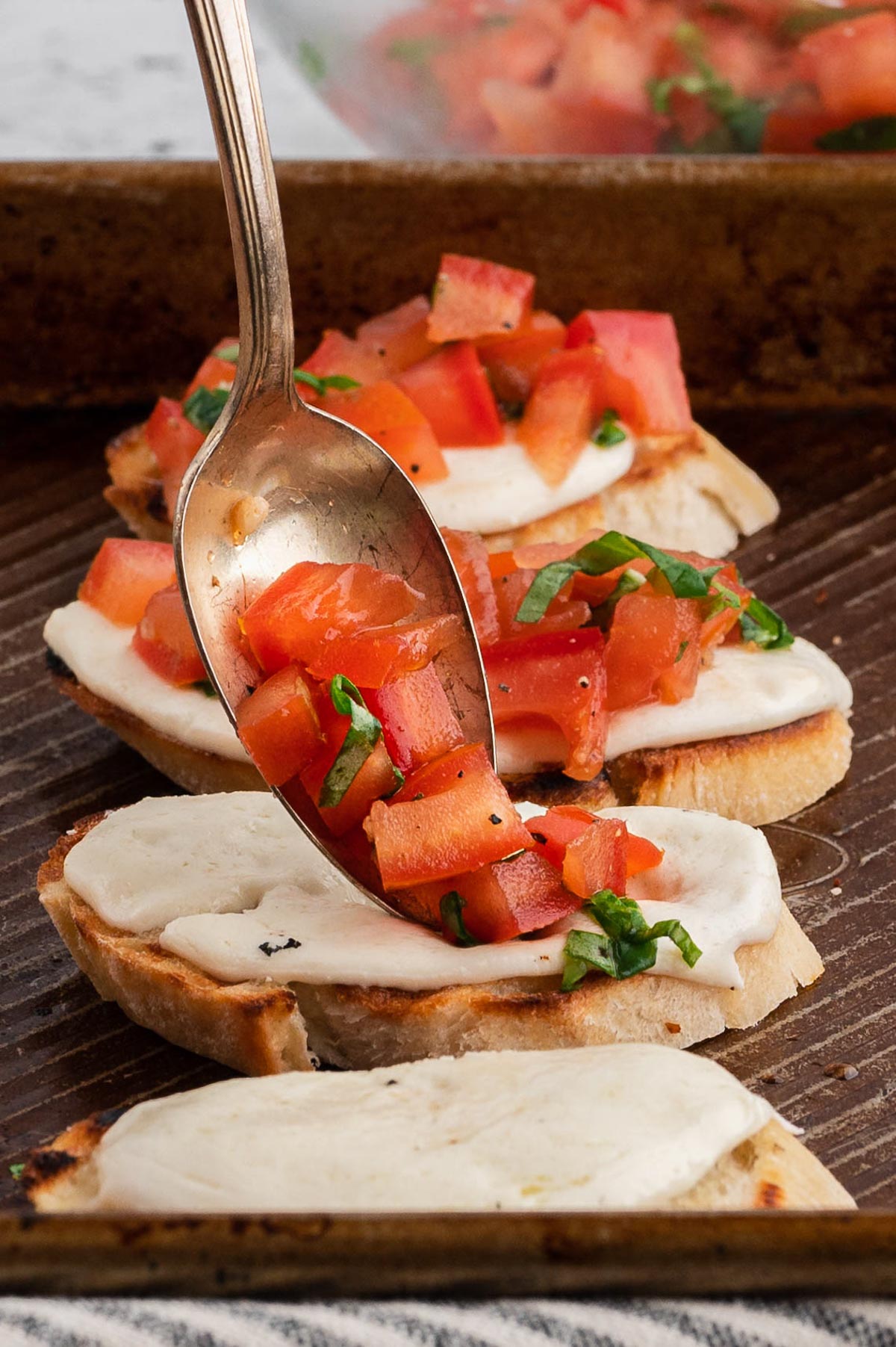 Mozarella on a piece of grilled baguetts, spooning tomato salad onto the baguette.