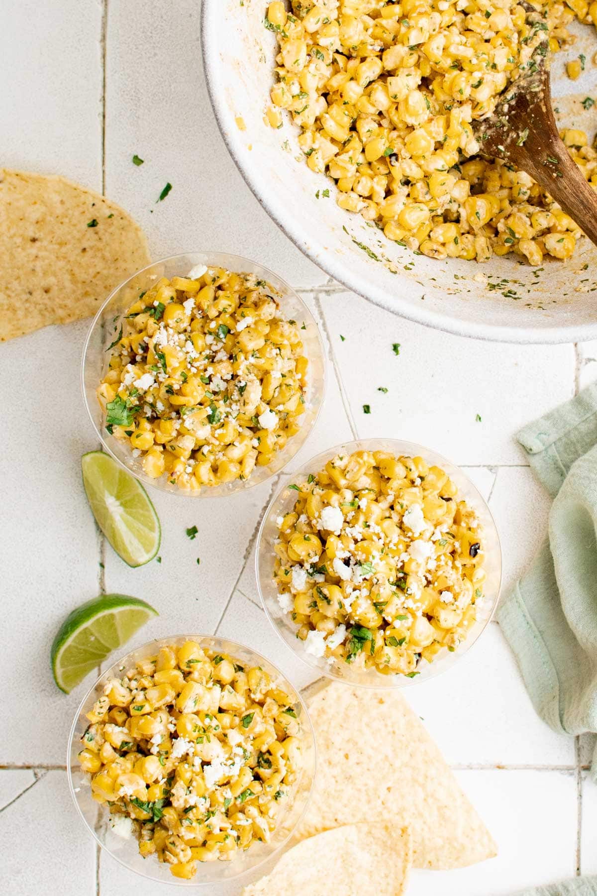 Elote in cups with tortilla chips and limes. 