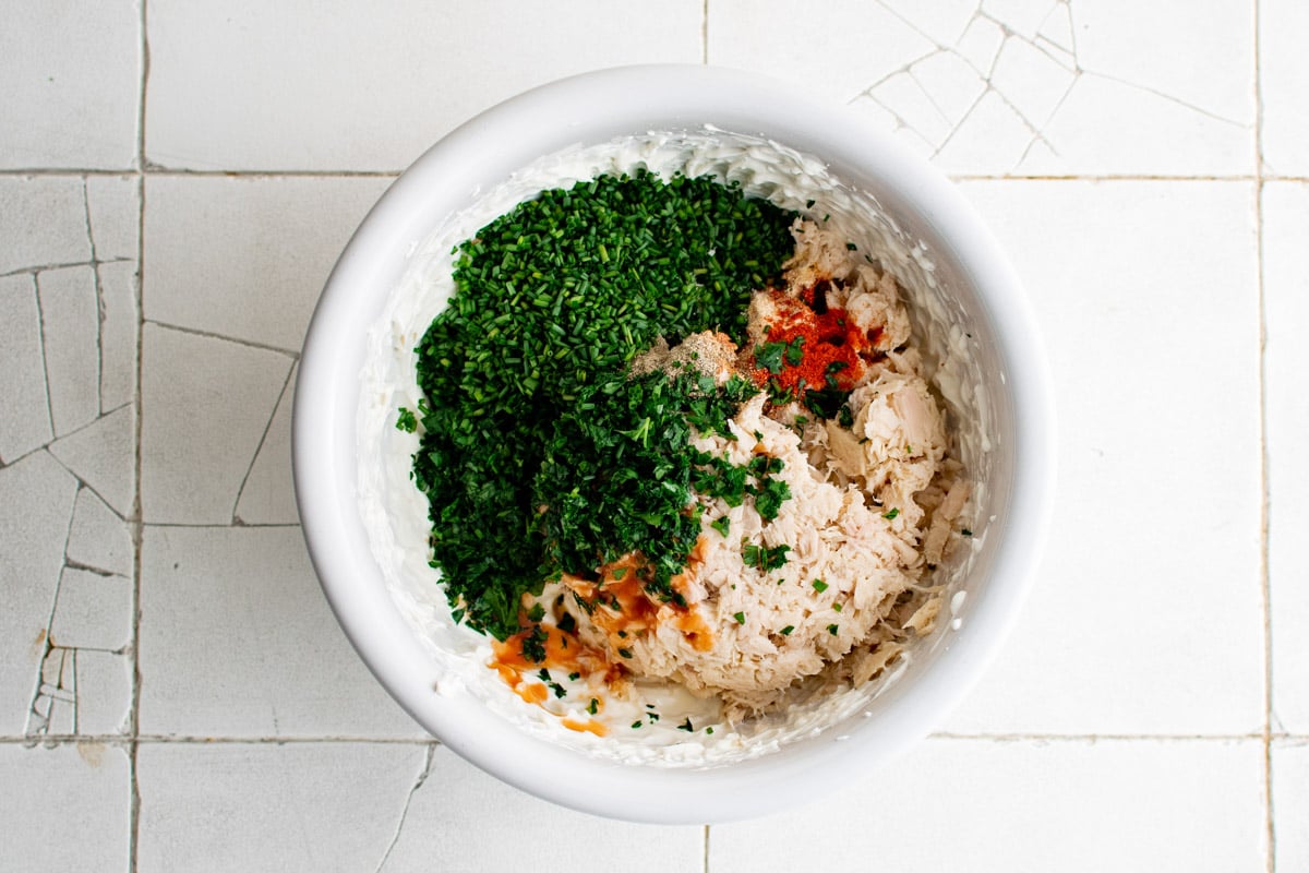 Cream cheese, seasoning, tuna and herbs in a white bowl.