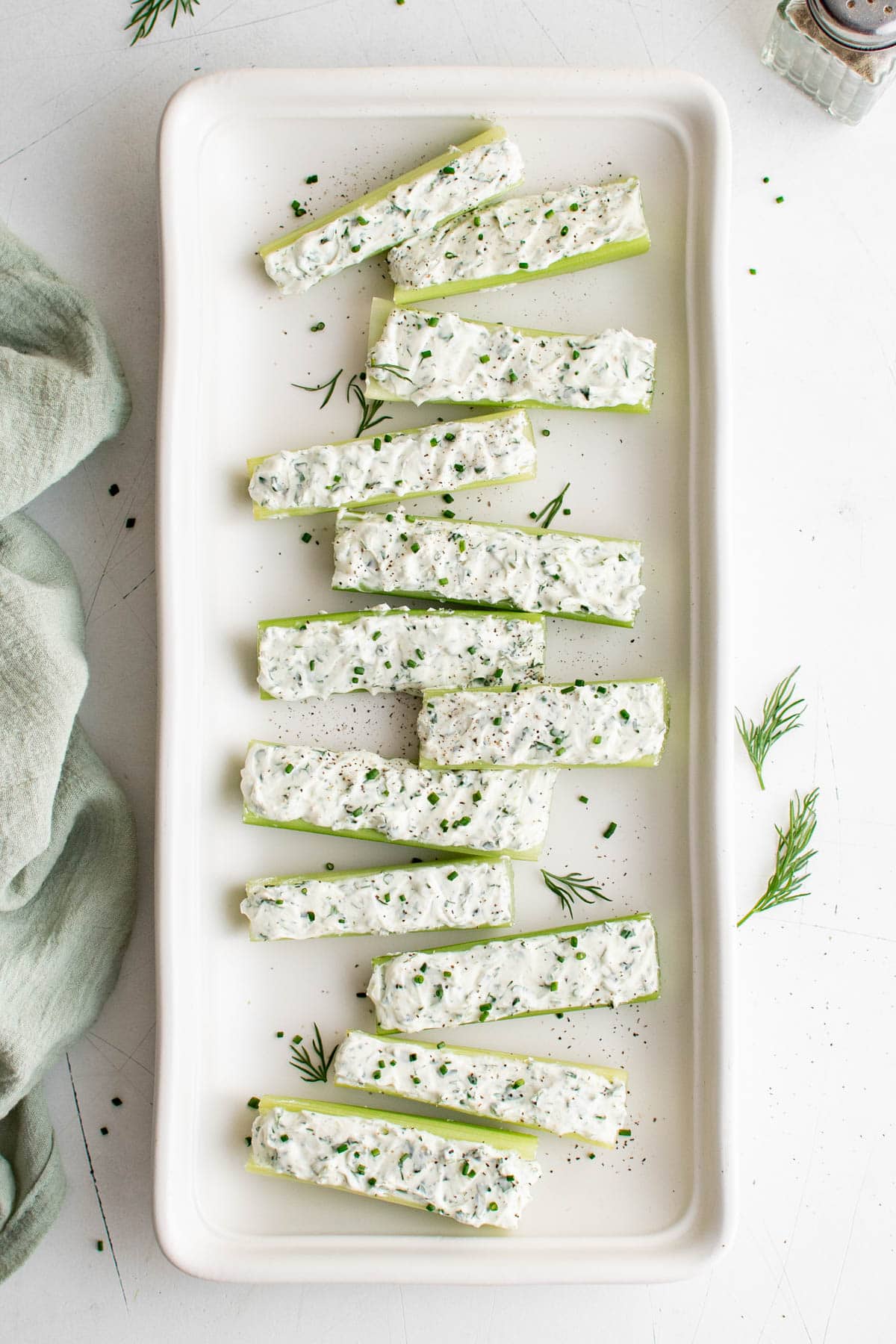 Celery sticks filled with herbed cream cheese on a white platter.