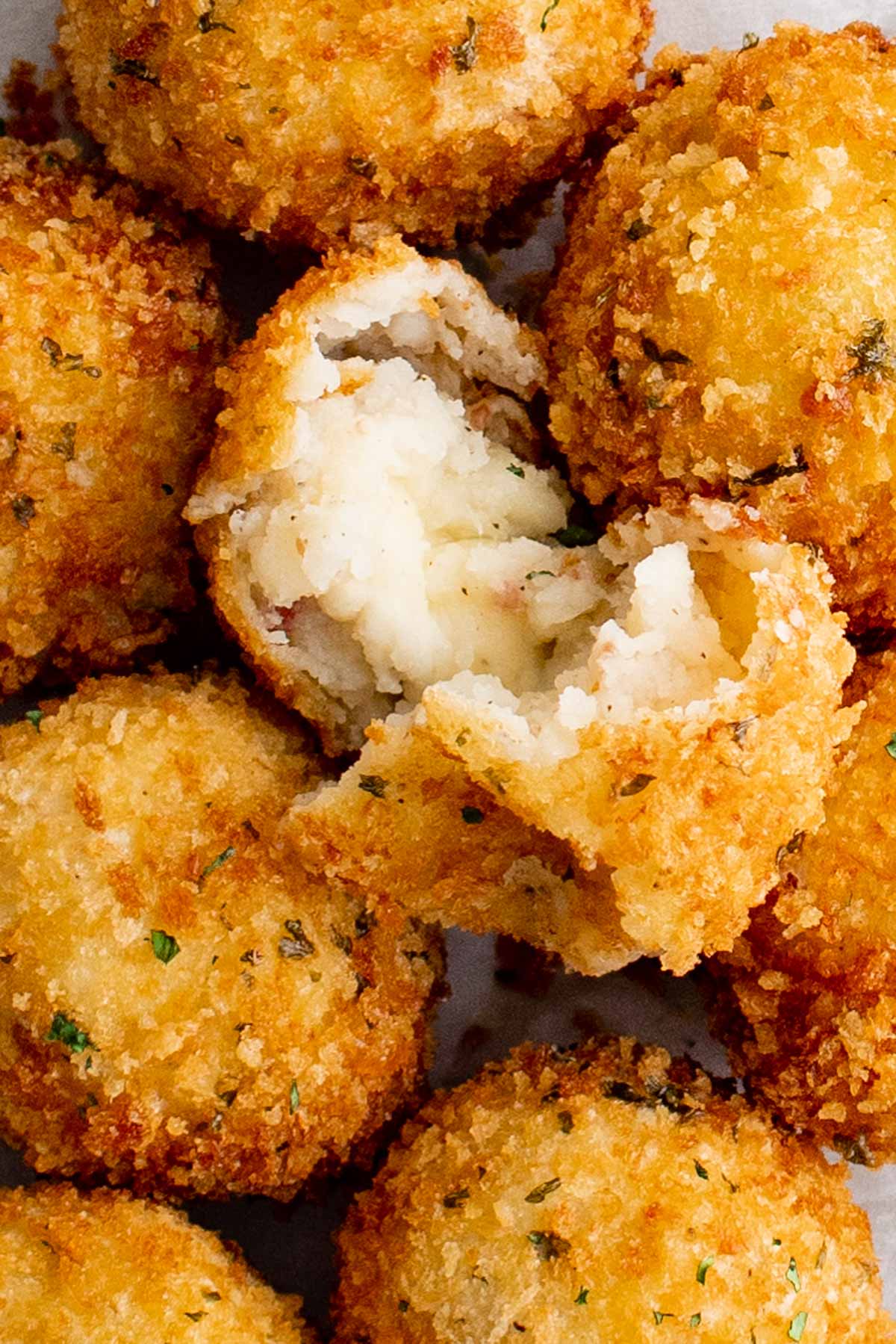 Close up of stack of fried potato balls with one on top split open.