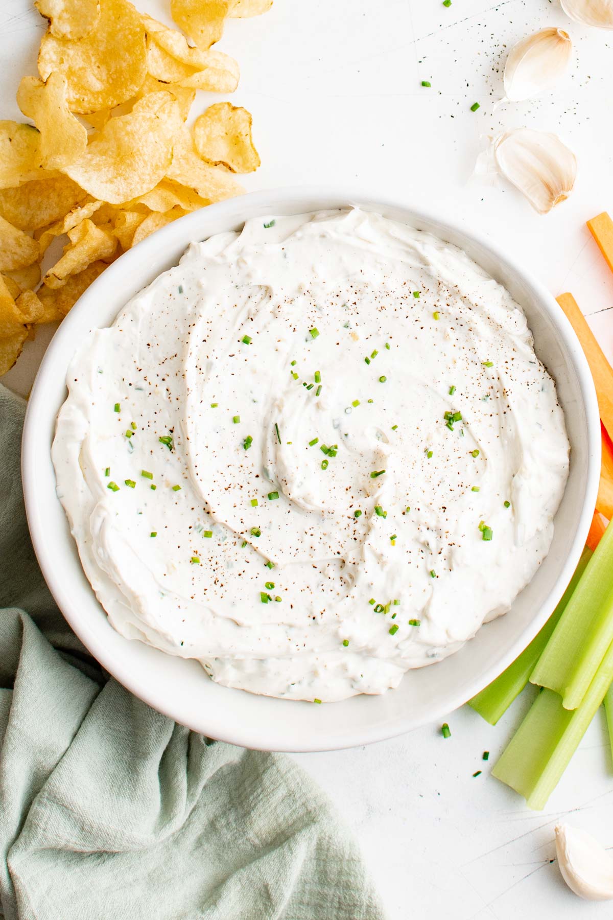 large bowl of garlic dip surrounded by potato chips and celery.