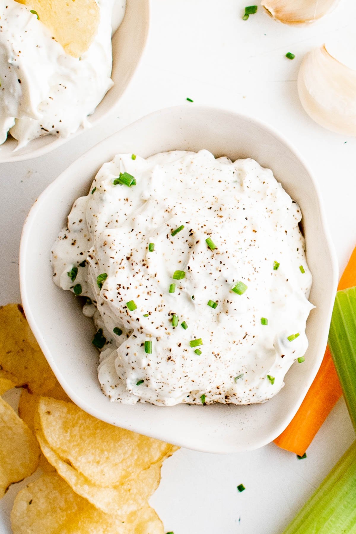 white bowl containing white garlic dip with chives and black pepper. 