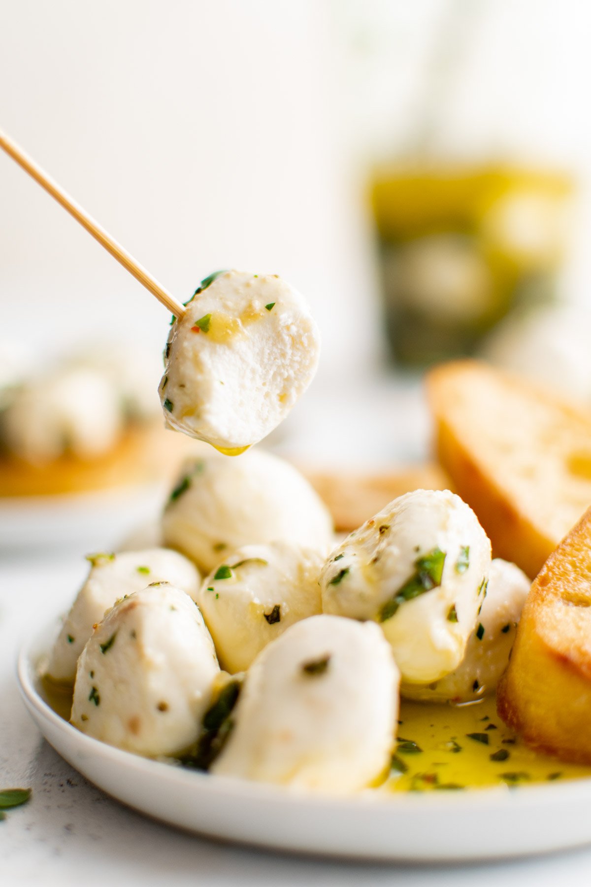 Mozzarella balls with herbs and olive oil with a toothpick on a plate.