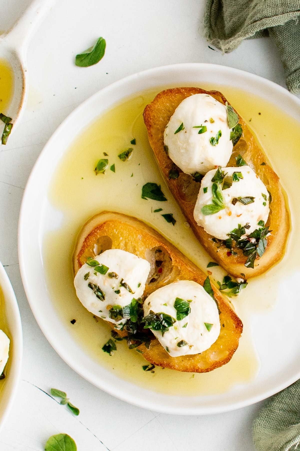 Crostini on a plate with marinated mozzarella with herbs and olive oil.