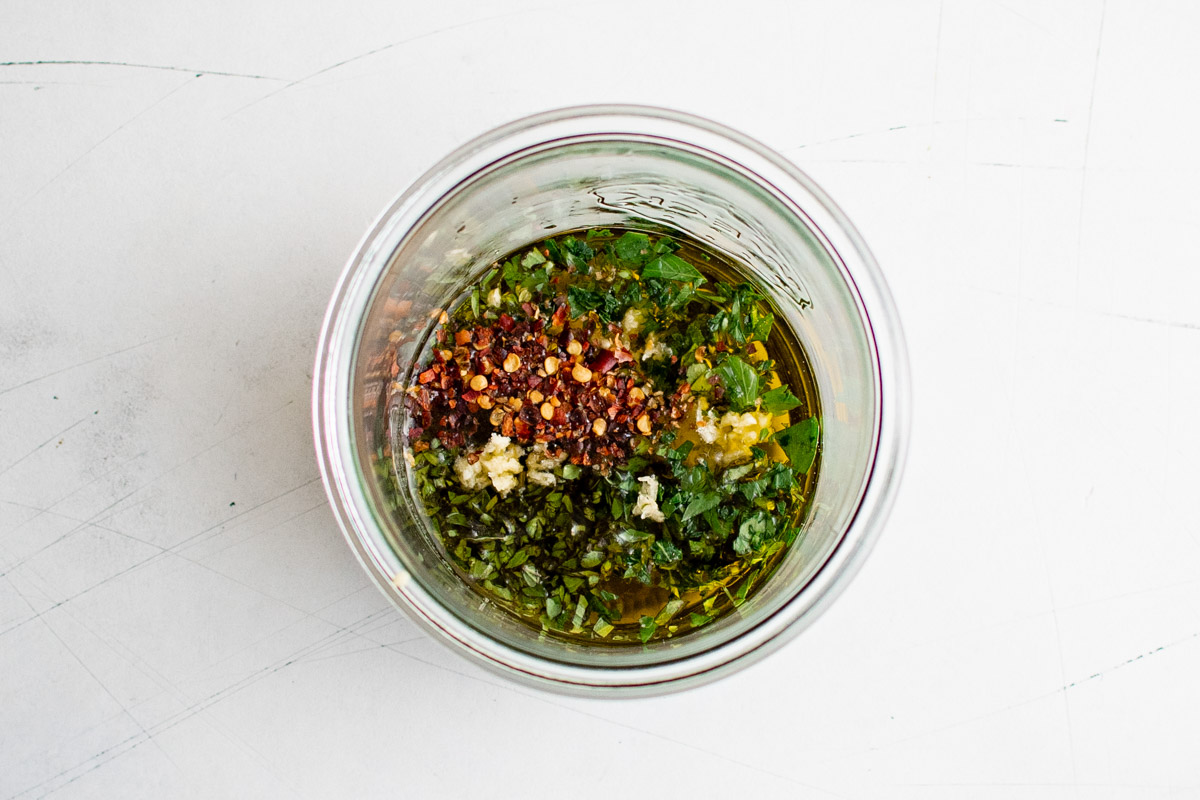 Fresh herbs and garlic with olive oil in a jar.
