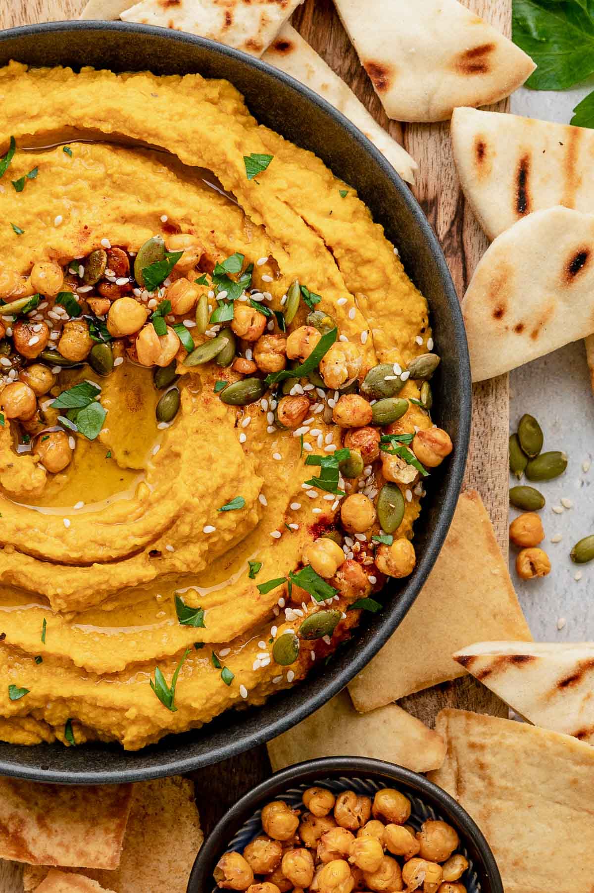A bowl of pumpkin hummus with naan and pita and chickpeas.