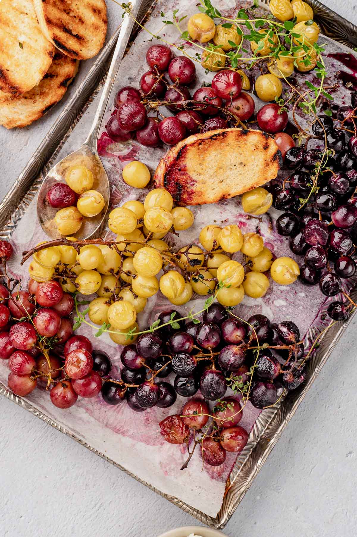 Roasted grapes on a baking sheet with toasted bread.