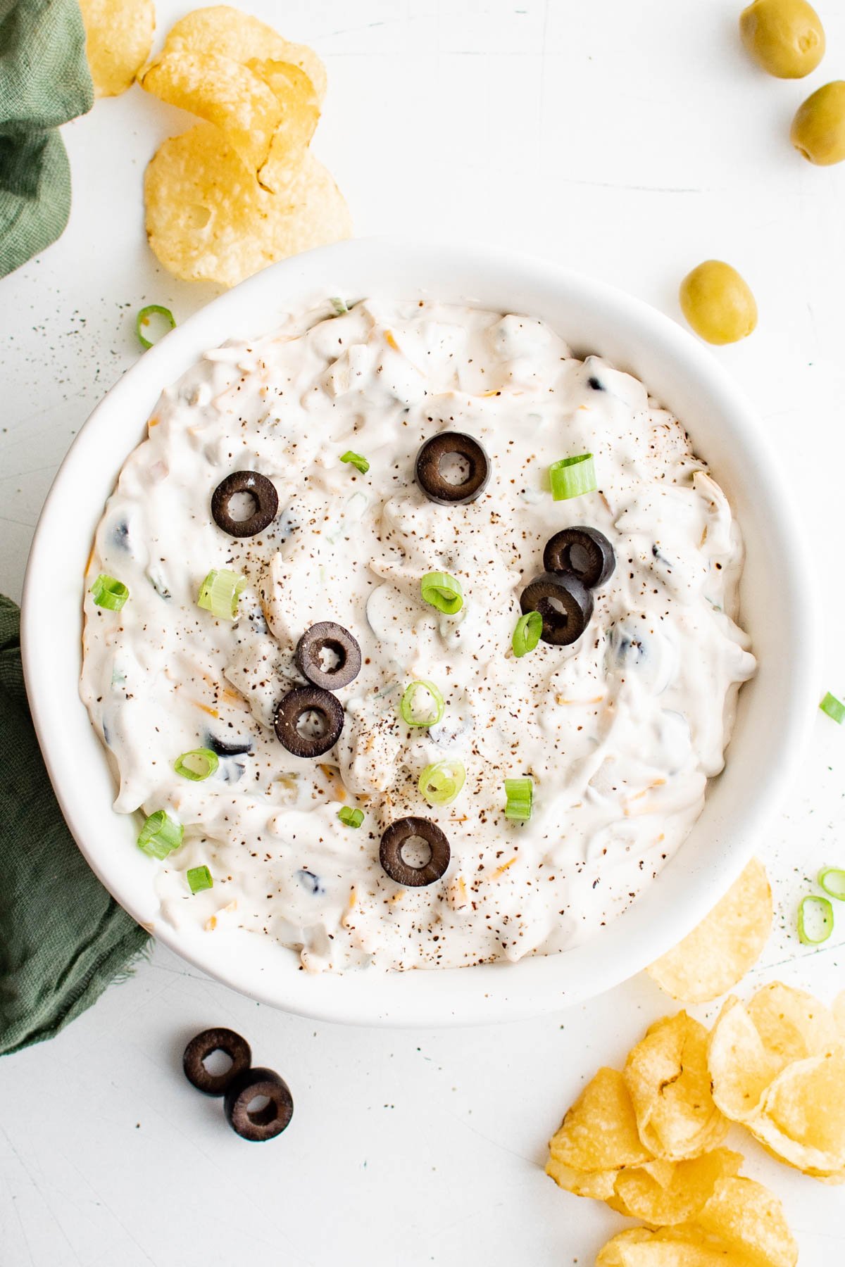 Olive dip in a white bowl surrounded by potato chips.