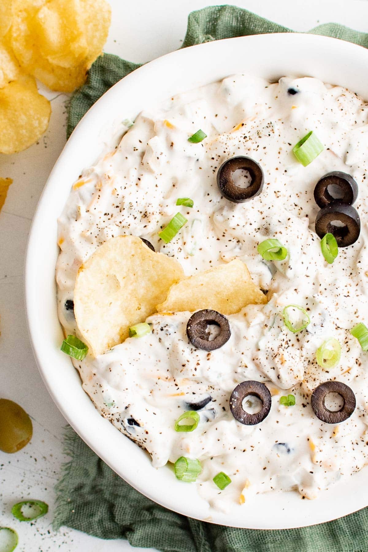 Creamy white dip with olives, green onions and black pepper garnish. Potato chips.