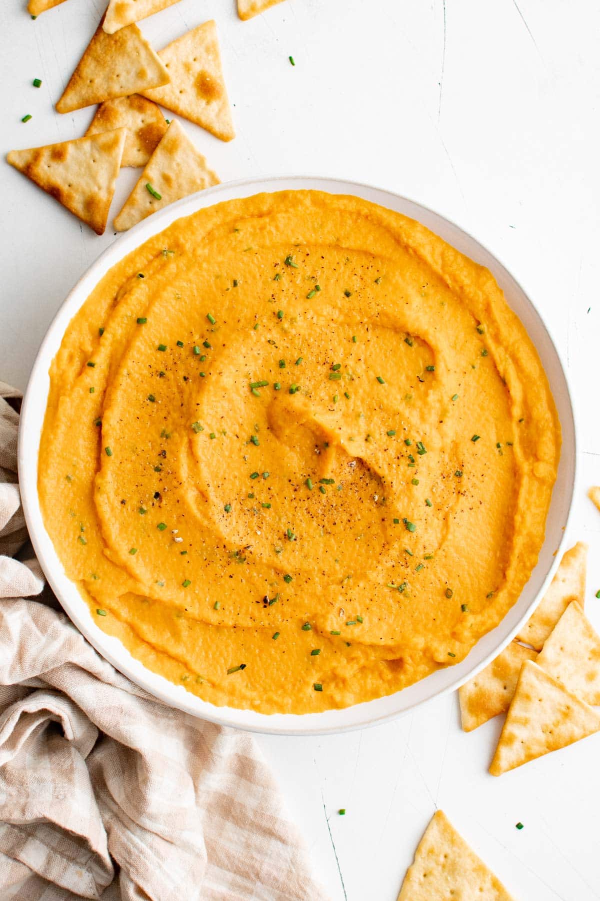 A large bowl of sweet potato dip with chives, and pita triangles scattered around