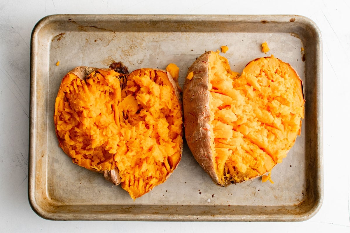 Two sweet potatoes on a baking sheet, sliced open and mashed.